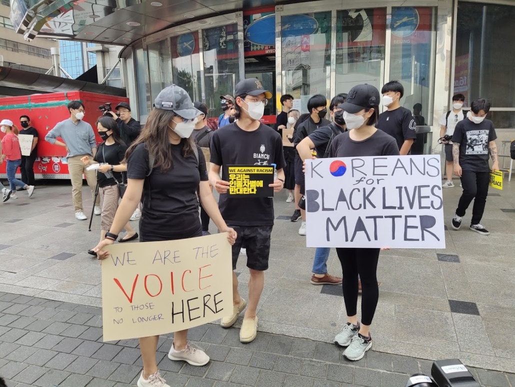 Photos of protesters at Black Lives Matters protest in Seoul, South Korea. They hold signs bearing "Koreans for Black Lives Matter," "We Against Racism" and "We are the voice to those no longer here" in English. 